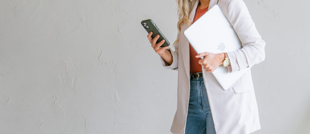 Person checking competitor messaging and offers on a phone while holding a laptop for brand positioning research.