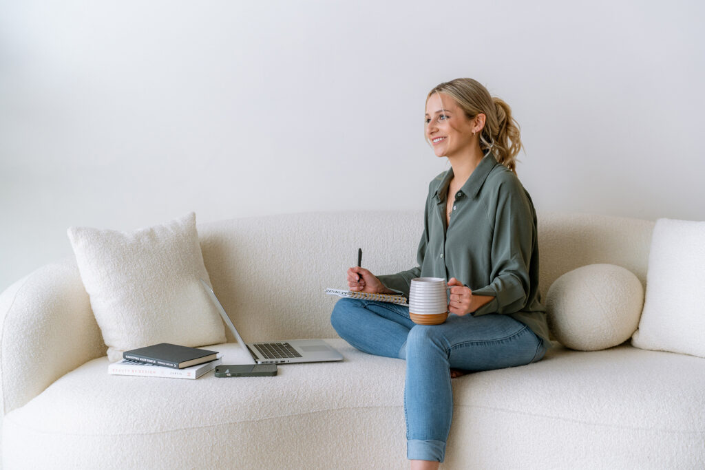Brand designer sitting on couch with laptop and notebook planning a complete brand identity system